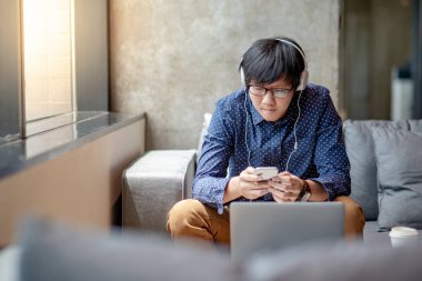 Mobil uygulama müzik dinlerken, oturma ve serbest zaman sırasında kanepede rahatlatıcı için Smartphone kullanan Genç Asyalı adam. Yaşam alanı kavramı kentsel yaşam tarzı
