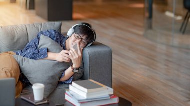 Mobil uygulama müzik dinlerken, yalan ve serbest zaman sırasında kanepede rahatlatıcı için Smartphone kullanan Genç Asyalı adam. Yaşam alanı kavramı kentsel yaşam tarzı