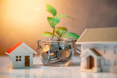 Gayrimenkul yatırım özelliği. Ev ipotek kredi oranı. Gelecekteki kavramı için para tasarrufu. Cam kavanoz ve ev modeli paralar dışarı masaya büyüyen yeşil bitki yansıması