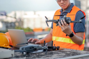 Genç Asyalı adam dron laptop ve smartphone inşaat alanında çalışma. İnsansız hava aracı (İHA) arazi için kullanarak ve inşaat mühendisliği proje sitesi anket oluşturma.