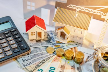 Gayrimenkul veya emlak geliştirme. İnşaat iş yatırım kavramı. Ev ipotek kredi oranı. Hesap makinesi, ev ve vinç ile uluslararası banknot para yığını masaya modelleri.