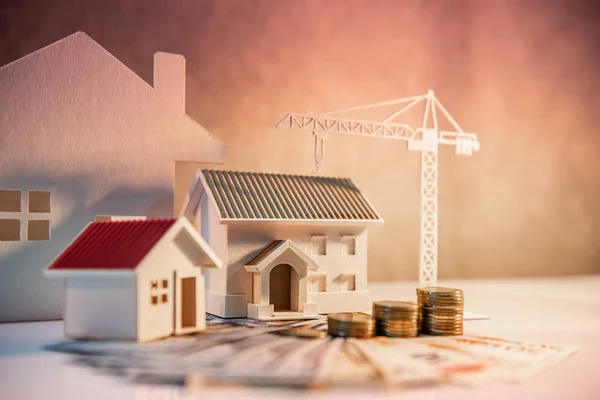 Real estate or property development. Construction business investment concept. Home mortgage loan rate. Coin stack on international banknotes with house and construction crane models on the table.