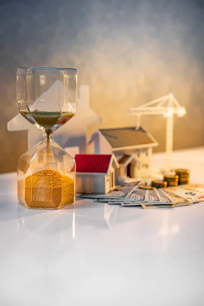 Real estate or property development. Construction business investment concept. Home mortgage loan rate. Coin stack on international banknotes with hourglasses, house and crane models on the table.