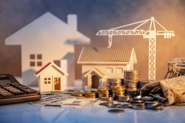 Real estate or property development. Construction business investment concept. Home mortgage loan rate. Coin stack on international banknotes with calculator, house and crane models on the table.