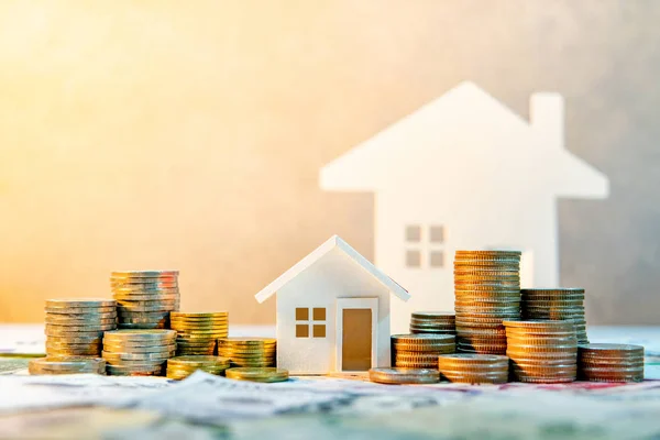 Real estate or property investment. Home mortgage loan rate. Saving money for retirement concept. Coin stack on international banknotes with house model on table. Business growth background