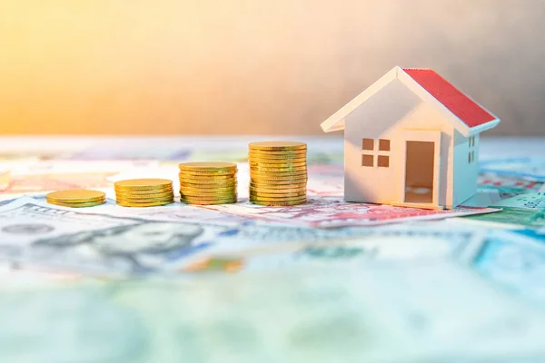 Real estate or property investment. Home mortgage loan rate. Saving money for retirement concept. Coin stack on various of international banknotes with house model on table. Business growth concept.
