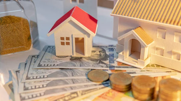 Real estate investment or property ladder concept. Home mortgage loan rate. Coin stack on international banknotes with hourglasses and house models on the table.