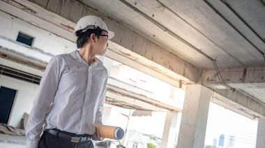 Asyalı erkek mühendis veya mimar planları veya inşaat alanında koruyucu güvenlik kask giyen süre mimari çizim tutmak. Mühendislik, Mimarlık ve inşaat kavramlar bina