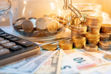 Hesap makinesi ile Döviz Alım cam kavanoz ve altın sikke yığını, dolar ve euro banknot masanın üzerinde. Bileşik faiz hesaplama veya finansal yatırım iş kavramları