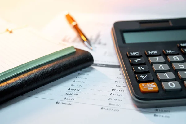 Calculator, pen, blank lined paper page of notebook and summary report paperwork with bar graph and table. Financial data analysis. Business planning and management concept