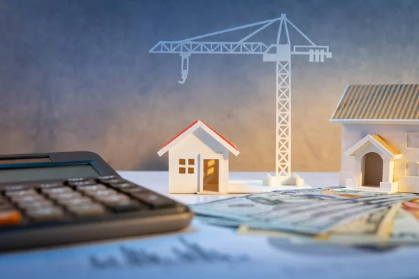 Real estate or property development. Construction business investment concept. Home mortgage loan rate. House and crane models on international banknotes with calculator on the table.