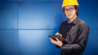 Küçük Asya adam giyen kişisel sarı koruyucu güvenlik kask yazma dijital tablet mühendislik. Mühendislik site kavramı üzerinde çalışma