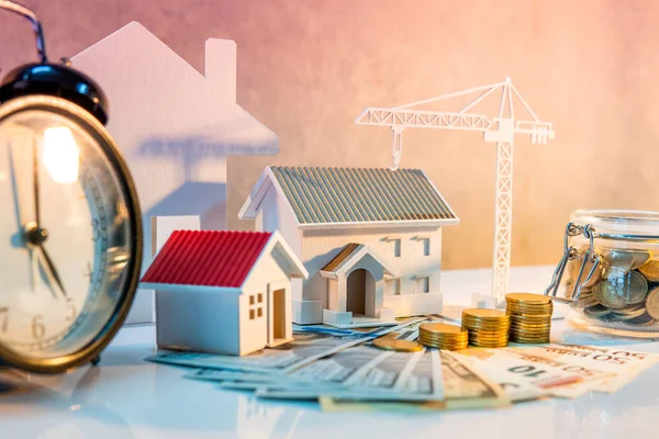 Real estate or property development. Construction business investment concept. Home mortgage loan rate. Coin stack on international banknotes with clock, house and crane models on the table.