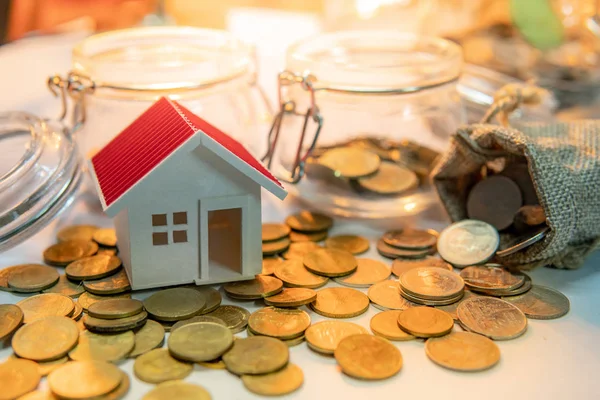 Property or real estate investment. Home mortgage loan rate. Saving money for future concept. House model with gold coins in currency glass jar and spilling out of money bag on the table