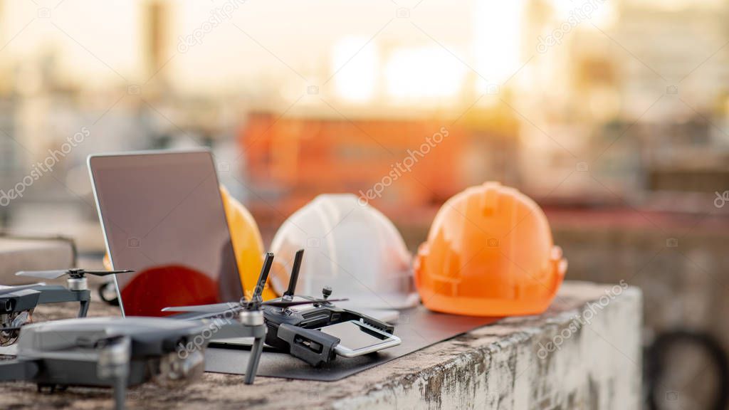 Drone, remote control, smartphone, laptop computer and protective helmet at construction site. Using unmanned aerial vehicle (UAV) for land and building site survey in civil engineering project.