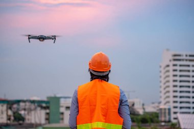Küçük Asya mühendis dron günbatımı sırasında inşaat sitesi üzerinden uçan adam. İnsansız hava aracı (İHA) arazi için kullanarak ve inşaat mühendisliği proje sitesi anket oluşturma.