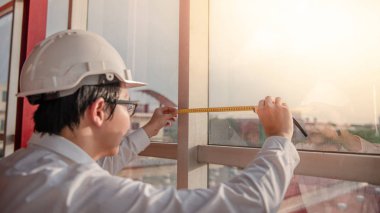 Küçük Asya mühendisi mezura (teyp ölçme) kullanan adam inşaat alanında, uzunluk ölçü aracı veya donanımları, Yapı İnşaat çalışma için pencere çerçevesi üzerinde
