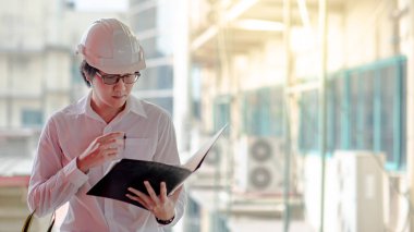 Asya mühendis veya mimar inşaat alanında kişisel koruyucu ekipman kask giyen süre dosyaları tutan. Mühendislik, Mimarlık ve inşaat iş kavramları