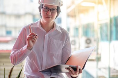 Genç Asyalı mühendis veya mimar inşaat alanında kişisel koruyucu ekipman kask giyen süre dosyaları tutan. Mühendislik, Mimarlık ve inşaat iş kavramları