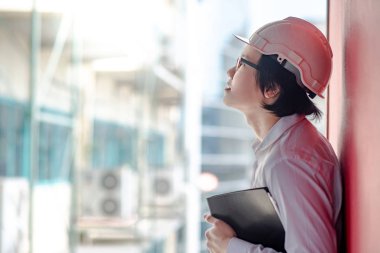 Genç Asyalı mühendis veya mimar inşaat alanında kişisel koruyucu ekipman kask giyen süre dosyaları tutan. Mühendislik, Mimarlık ve inşaat iş kavramları