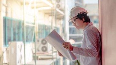 Genç Asyalı mühendis veya mimar inşaat alanında kişisel koruyucu ekipman kask giyen süre dosyaları tutan. Mühendislik, Mimarlık ve inşaat iş kavramları