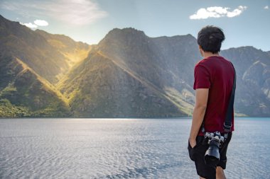 Genç Asyalı adam fotoğrafçı South Island Yeni Zelanda dağ ve göl sahne bakarak. Seyahat ve manzara fotoğrafçılığı kavramları