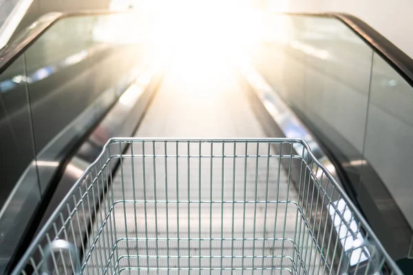 Empty metal shopping cart (trolley) on travelator or escalator in supermarket or grocery store. Shopping lifestyle concept