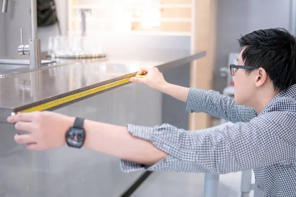 아시아인 청년은 현대식 진열실의 화강암 반월판을 측정하는 테이프를 사용하였다 가구를 — 스톡 사진
