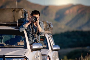 Genç Asyalı erkek yolcu ve araç penceresi alarak fotoğraf yolu üzerinde oturan fotoğrafçı Namibya Afrika gezisi. Seyahat fotoğraf kavramı