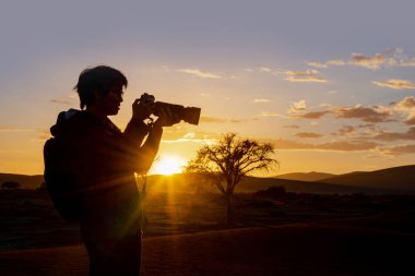 Fotoğrafta gündoğumu sırasında Namibya, Afrika Namib Çölü'erkek Asya fotoğrafçı siluet vurdu. Seyahat fotoğraf kavramı