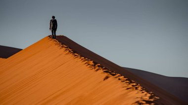 Genç erkek seyyahı ve fotoğrafçı kumul üst kısmında Namib Çölü, Namibya, Afrika'da gündoğumu sırasında ayakta. Seyahat fotoğraf kavramı