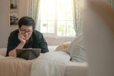 Rahat yatak yatakta yatan ise dijital tablet ve kalem kullanan genç Asya iş adam. Ev yaşam yaşam tarzı modern elektronik aygıtı kavramı ile