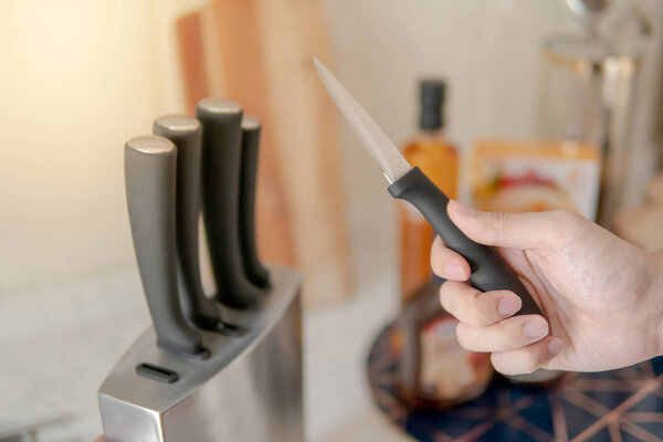 Male hand choosing knife from the set on vintage kitchen counter. Home living lifestyle in the kitchen.