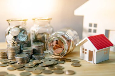 Para dolu cam kavanozlarda para ve ahşap masaya dökülmüş ev modelleri. Gelecekteki emeklilik için para biriktiriyorum. Ev kredisi oranı. Gayrimenkul geliştirme veya emlak yatırım kavramı