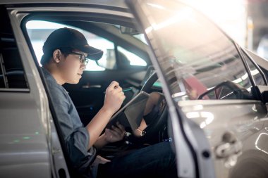 Otomatik hizmet garajda dijital tablet kullanarak araç deneme sürücü koltuğuna oturan Asya otomatik mekanik. Otomotiv endüstrisinde çalışan mekanik bakım mühendisi. Otomobil Bakımı ve onarımı