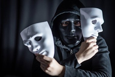 Mystery hoody man wearing black mask holding two white masks in his hand. Anonymous social masking. Major depressive disorder or bipolar disorder. Halloween concept clipart