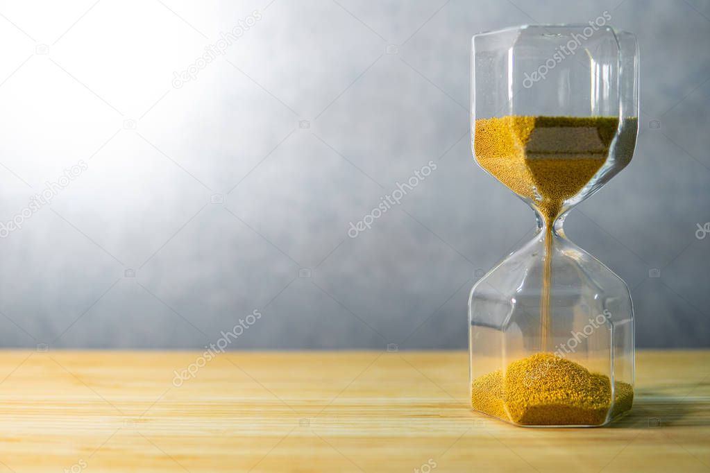 Gold sand running through the shape of modern hourglass on wooden table.Time passing and running out of time. Urgency countdown timer for business deadline concept