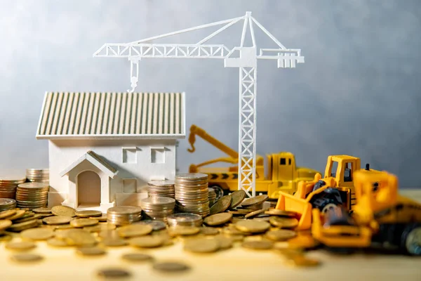 House, crane and construction truck models with gold coins spilling on wooden table. Real estate development or property investment. Home mortgage loan rate. Construction industry business concept