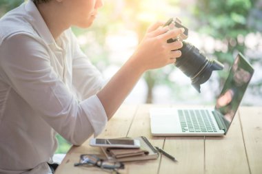 Küçük Asya holding tek objektifli dijital refleks fotoğraf makinesi (Dslr) kontrol resmi için kamera perde göstermek ile dizüstü bilgisayar ve smartphone masada oturan adam. Fotoğrafçılık, sanat ve hobi kavramları