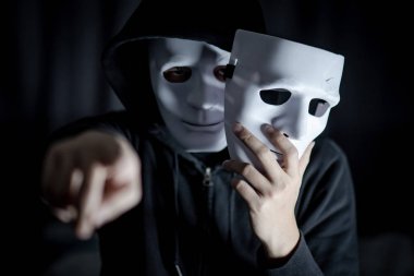 Elini işaret ve kırık beyaz maske tutan gizemli hoody adam. Anonim sosyal maskeleme. Major depresif bozukluk ya da bipolar bozukluk. Cadılar Bayramı kavramı