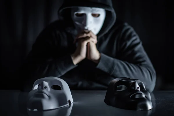 戴着神秘面具的连帽衫男士在桌子上选择黑色或白色面具 匿名社交屏蔽 主要抑郁症或躁郁症 万圣节概念 — 图库照片