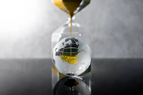 在桌子上的世界水晶玻璃的沙漏形状的黄金沙子的反映 全球可持续发展事业 环境保护 时间传递概念 — 图库照片