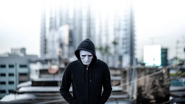 Mystery hoodie man in white mask standing in the rain on rooftop of abandoned building. Bipolar disorder or Major depressive disorder. Depression concept