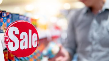 Süpermarketteki ürün rafında kırmızı etiket ve arka planda yiyecek paketini seçen bulanık bir erkek var. Market konseptinde alışveriş yaşam tarzı