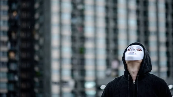 Mystery hoodie man in white mask standing in the rain looking up at the sky on rooftop of abandoned building. Bipolar disorder or Major depressive disorder. Depression concept