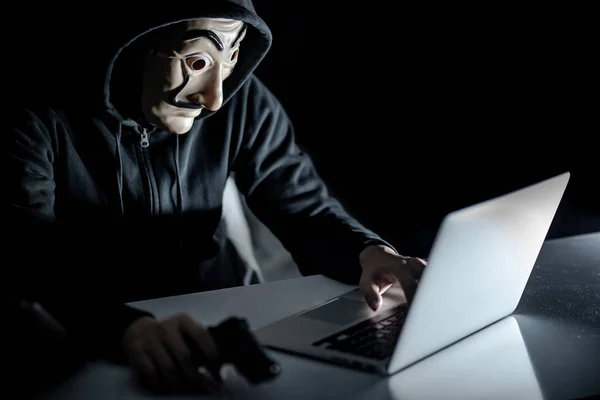 Hoodie hacker segurando arma sentado com laptop — Fotografia de Stock