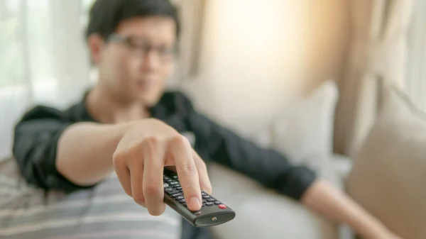 Asian man using remote controller while watching TV