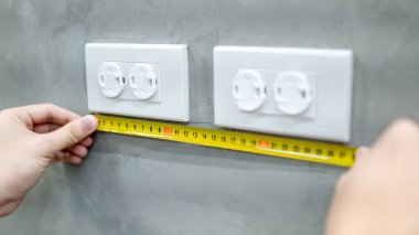 Erkek el elektrikçi elektrik prizine emniyet kapak Duvar ile boyutunu ölçmek için mezura kullanarak. Elektrik fikstür yükleme ve bina inşaat kavramlar