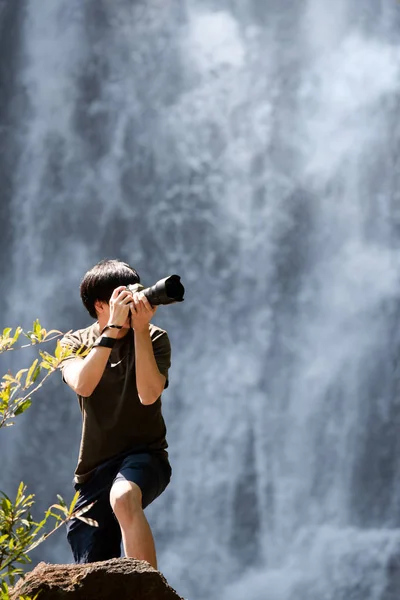 亚洲男人旅行者和摄影师使用数码相机在瀑布拍照 旅行生活方式或自然摄影概念 — 图库照片
