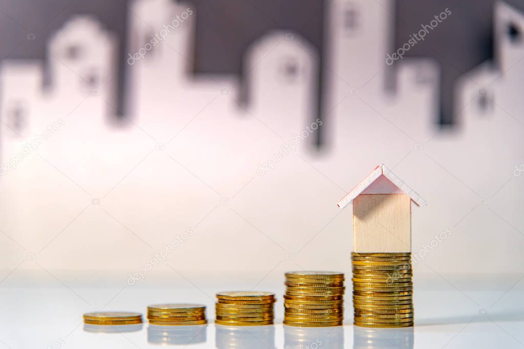 Real estate investment or Home mortgage loan rate. Property ladder concept. Coins stack and house model on the table with white city background. Money investing and business growth.